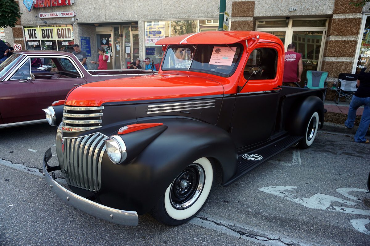 A red and black 1941 Chevrolet pickup parked on a small-town main street