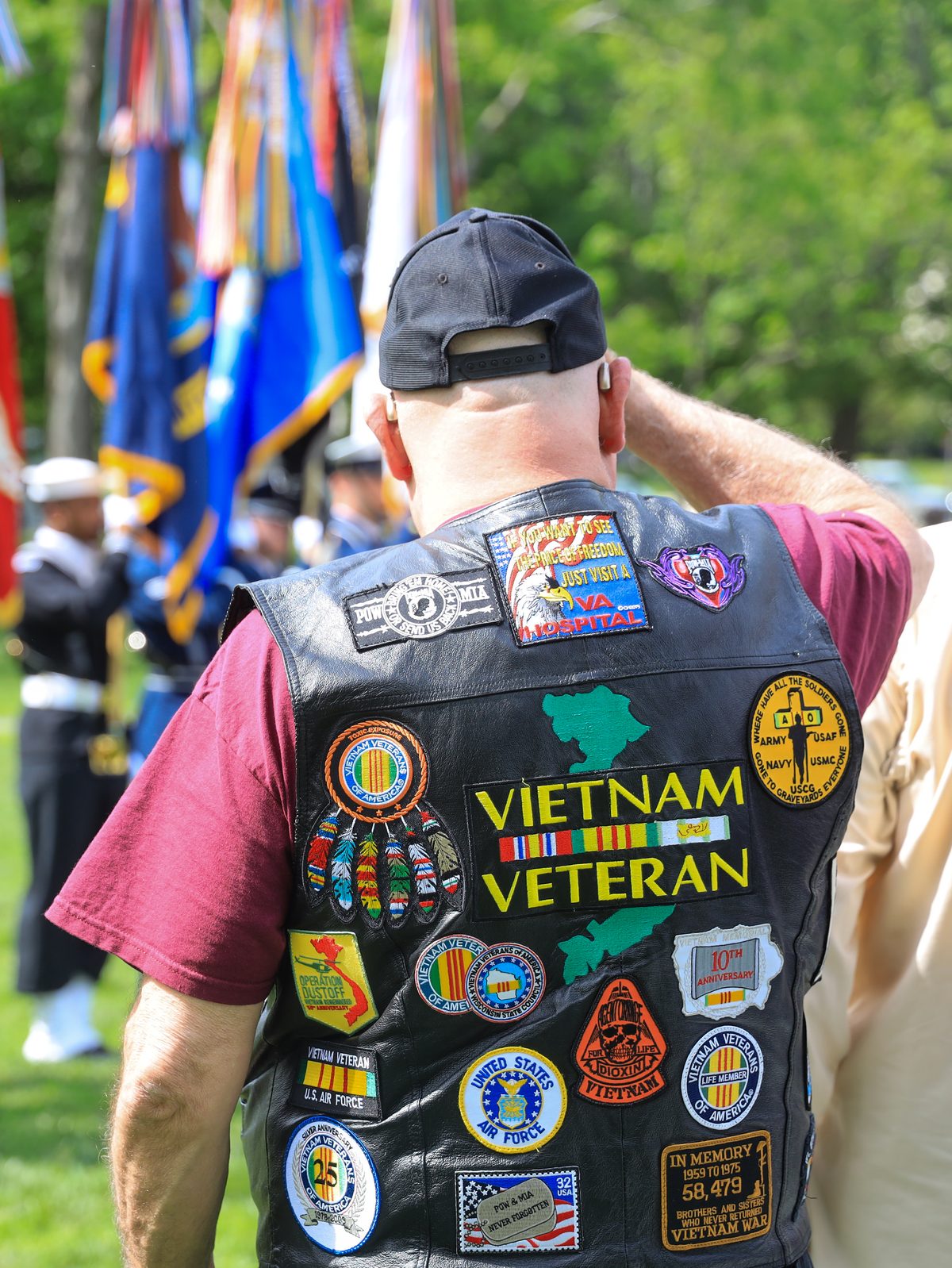 A Vietnam veteran, seen from behind in a patch-covered vest, saluting at the Vietnam Veterans Memorial